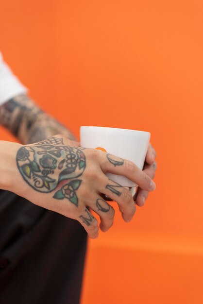 Вид сбоку человека с татуировками, держащего чашку кофе в кафе