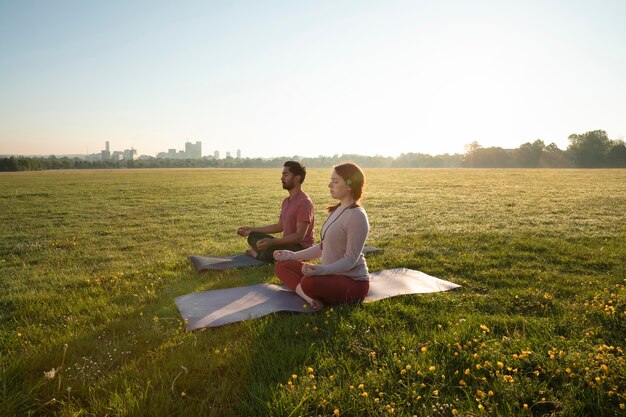 Side view of man and woman meditating outdoors on yoga mats