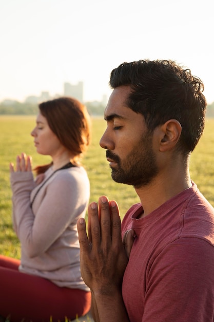 Мужчина и женщина, медитирующие на открытом воздухе, вид сбоку