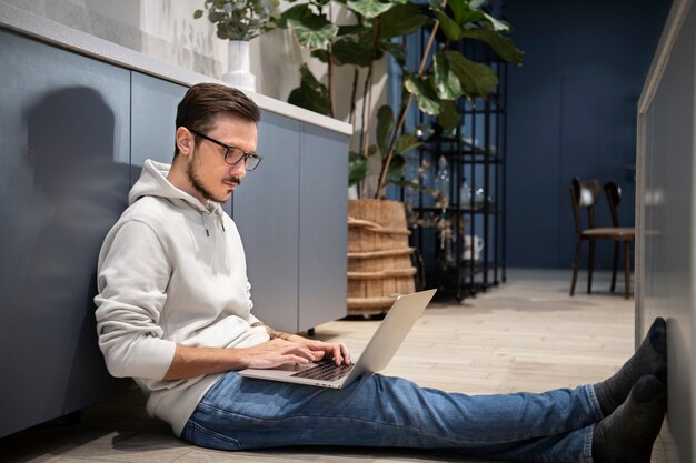 노트북과 함께 바닥에 앉아있는 동안 집에서 일하는 남자의 측면보기