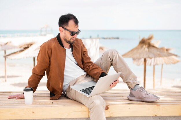 Вид сбоку человека, работающего на ноутбуке на пляже