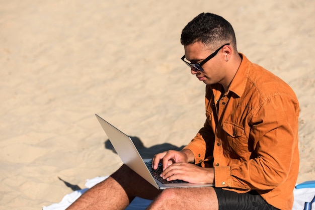 Vista laterale dell'uomo che lavora al computer portatile in spiaggia