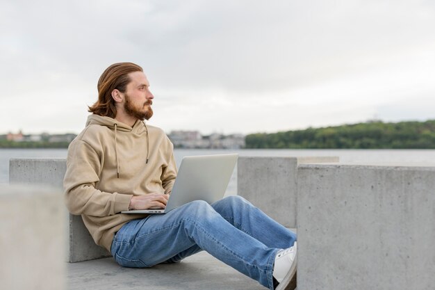 Side view of man working on laptop next to lake