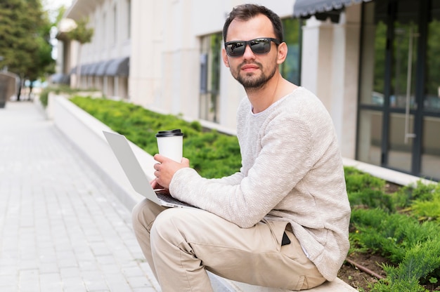 Side view of man working outside with laptop and coffee