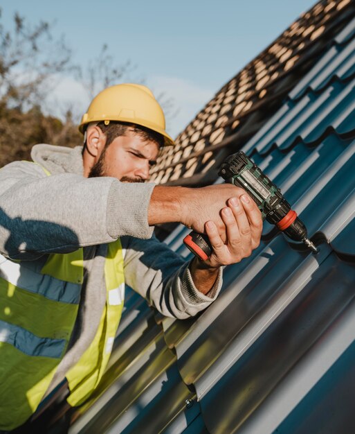 Side view man working on roof with a drill