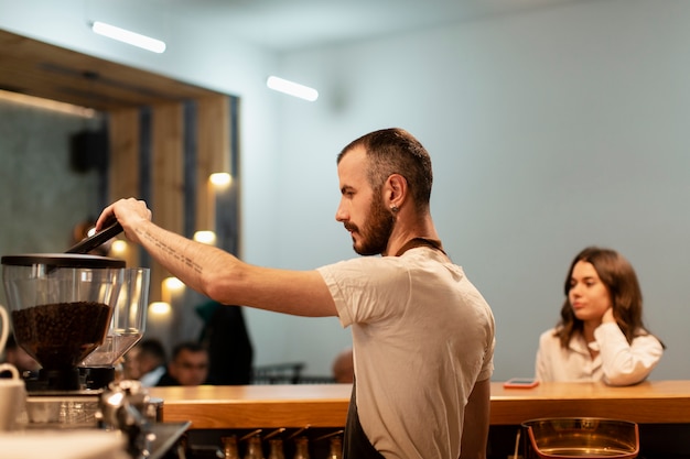 Free photo side view of man working in shop and making coffee