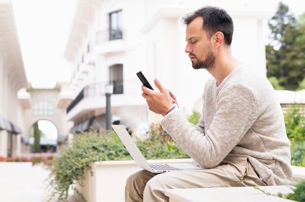 Side view of man working on smartphone and laptop outdoors