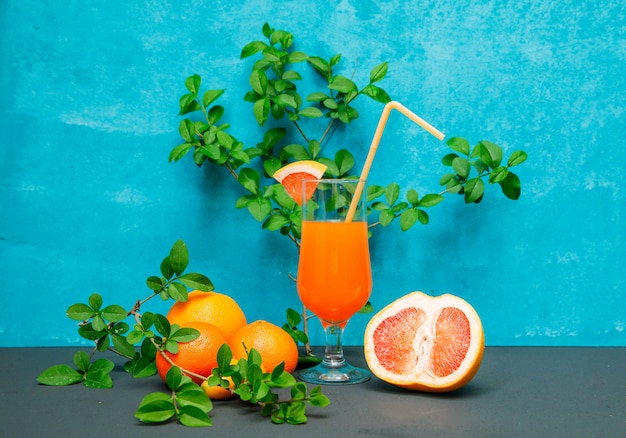 Side view mandarin oranges with leaves, orange and juice on blue textured surface. horizontal