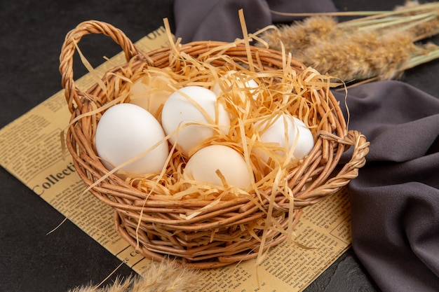 Side view of many organic eggs in a basket on an old newspaper on black towel on dark background