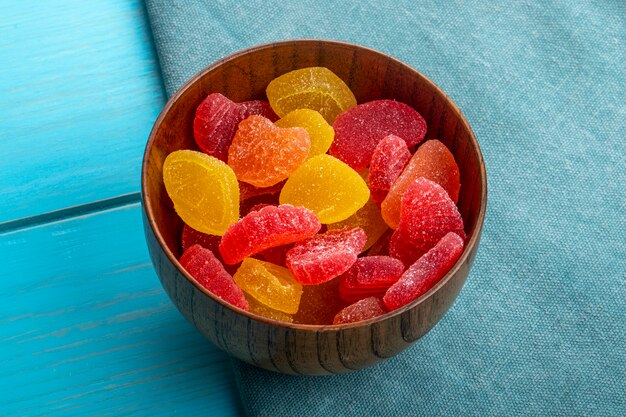 Side view of marmalade candies in a wooden bowl on blue