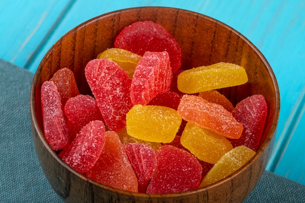 Side view of marmalade candies in a wooden bowl on blue