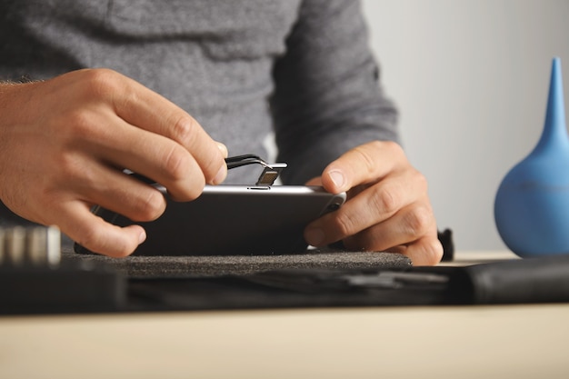 Side view, master uses pincher tool to remove sim card slot from smart phone while disassembling it