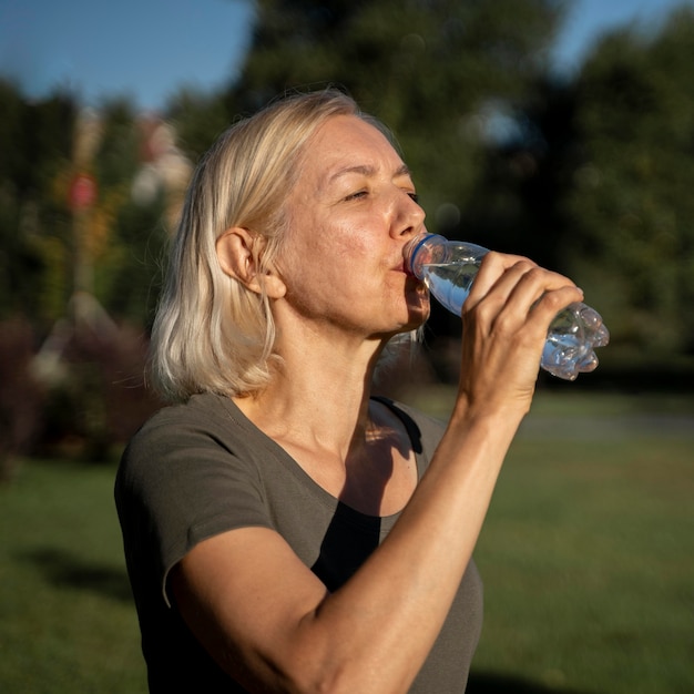 Free photo side view of mature woman drinking water outdoors