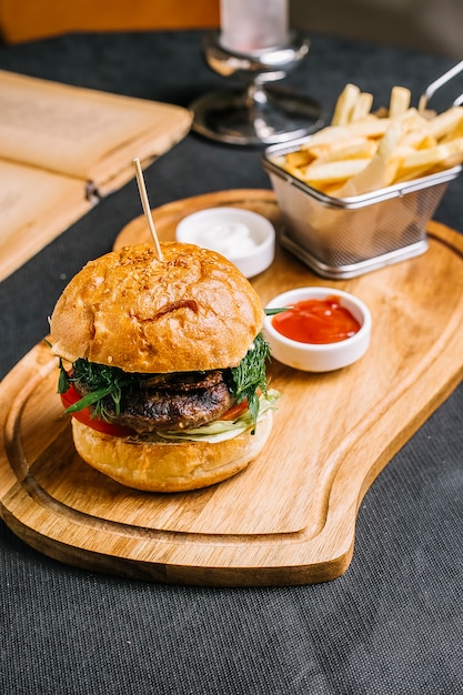 フライドポテトのマヨネーズとプレート上のケチャップとハンバーガーのパンのビーフパティトマトグリーンレタスとサイドビュー肉ハンバーガー