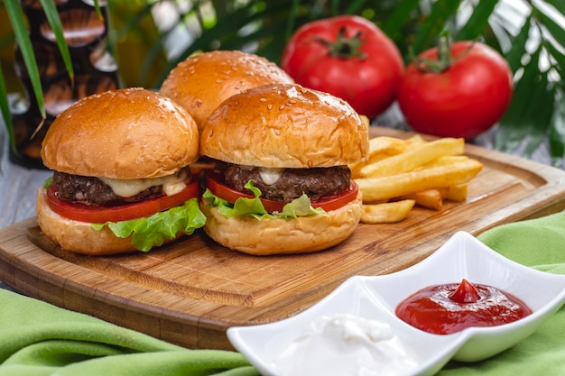 Side view meat burgers with french fries ketchup and mayonnaise on the board