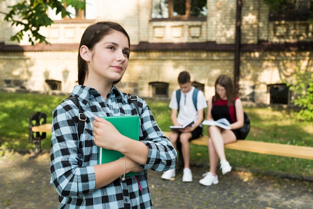 Side view medium shot of dreamy highschool girl holding notebook