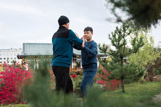 Foto gratuita uomini di vista laterale che praticano il tai chi all'esterno