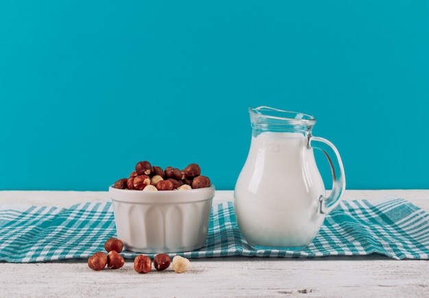 Side view milk carafe with bowl of almonds on white wooden and blue cloth background. horizontal space for text