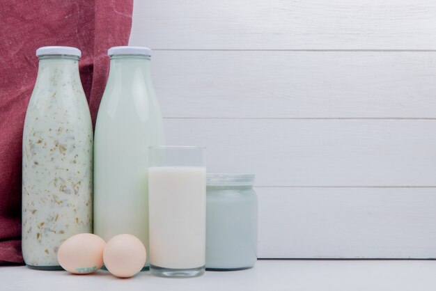 side view of milk products as azerbaijani yogurt soup milk and sour clotted milk with eggs on white surface and wooden table with copy space