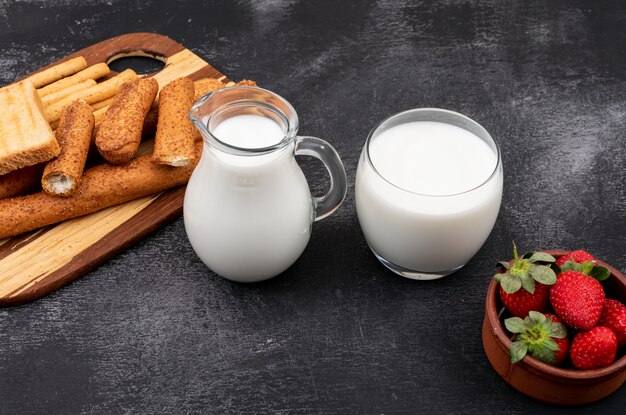 Side view of milk with crackers and strawberry on black surface horizontal