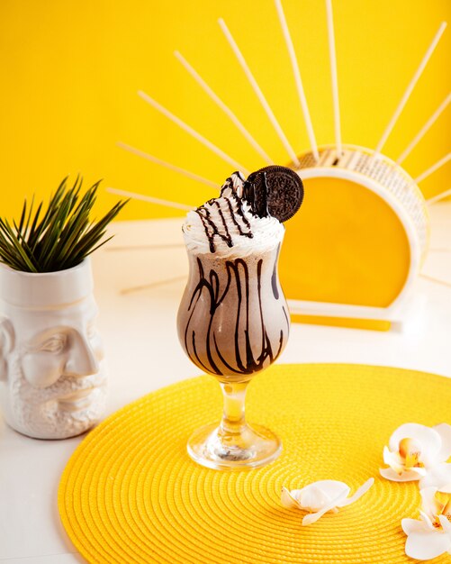 Side view of milkshake with whipped cream and cookie in glass on yellow