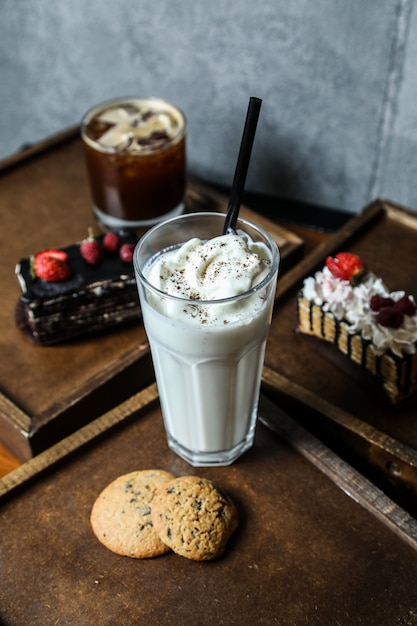Side view milkshake with whipped cream in a glass with cookies on a tray