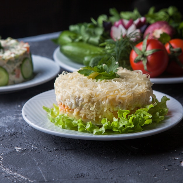 Foto gratuita insalata della mimosa di vista laterale con insalata e pomodoro e cetriolo più olivier in piatto bianco rotondo