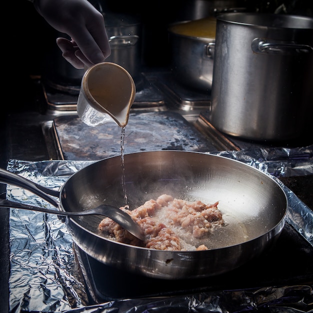 Side view minced meat with pan and water and human hand in stove