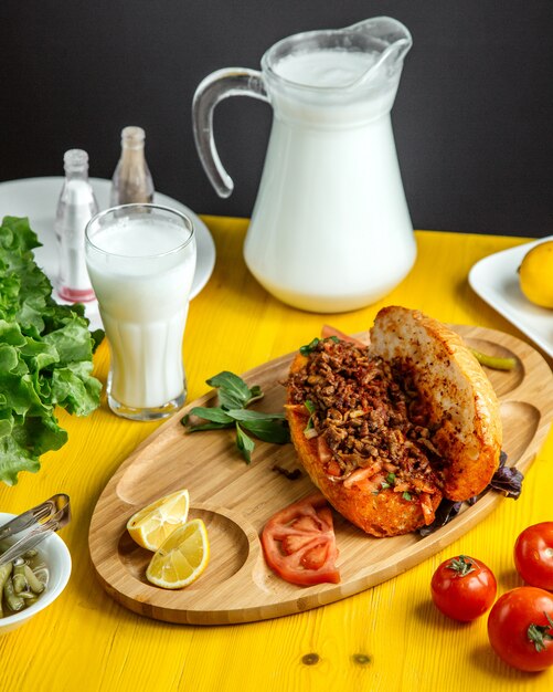 Side view of minced meat with vegetables in bread served with fresh tomatoes and lemon on wooden board