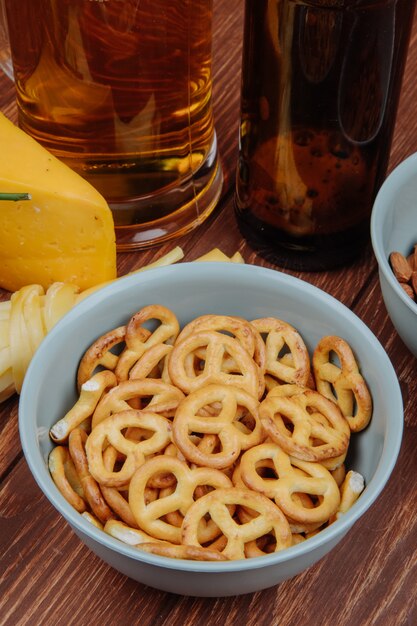 Side view of mini pretzels in a bowl and cheese with beer on rustic