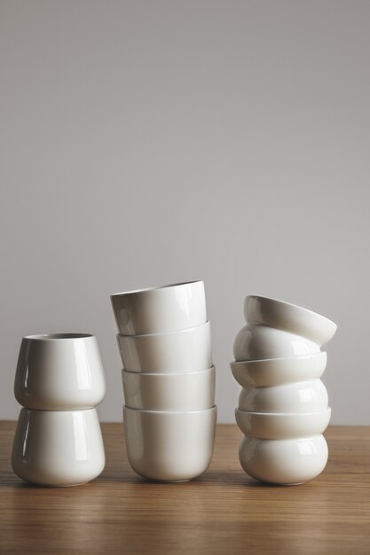 Side view mix of different blank white simple coffee cups in pyramide on thick wooden table isolated