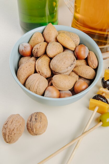 Side view of mix of nuts in a bowl with beer on white