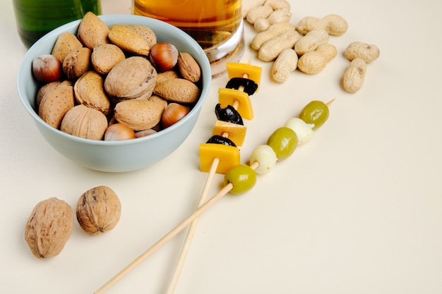 Side view of mix of nuts in a bowl with pickled olives and beer on white with copy space