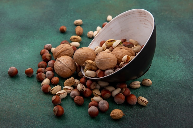 Side view of mix of nuts walnuts pistachios hazelnuts and peanuts in a bowl on a green surface