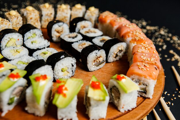 Side view mix sushi rolls with avocado sesame seeds and chopsticks on a stand