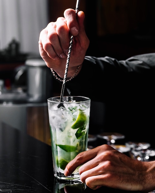 Вид сбоку коктейль ром Мохито с лаймом, мятой и льдом в бокале