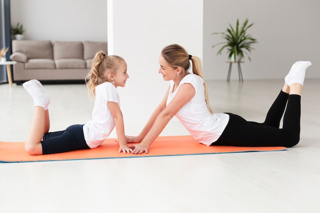Side view of mother and daughter exercising on yoga mat at home