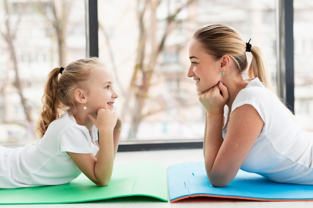 Side view of mother and daughter posing at home on yoga mat