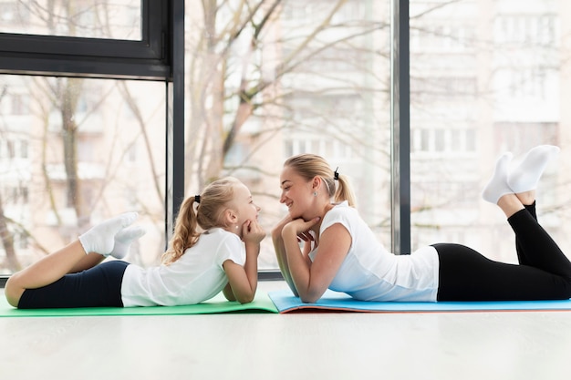 Side view of mother and daughter posing on yoga mat