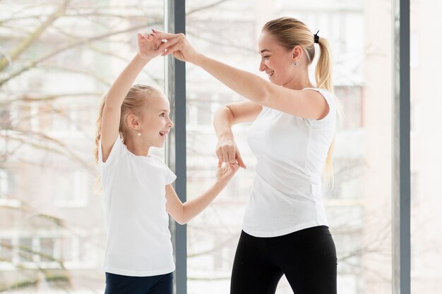 Side view of mother exercising at home with smiley daughter