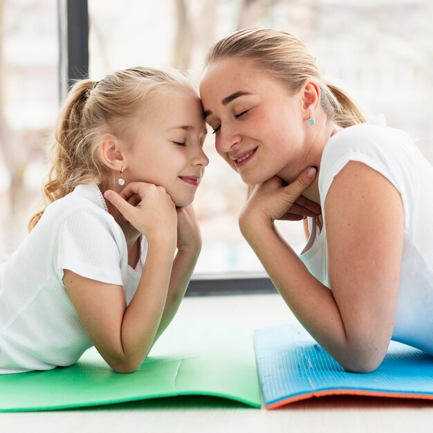 Side view of mother posing on yoga mat with daughter while at home