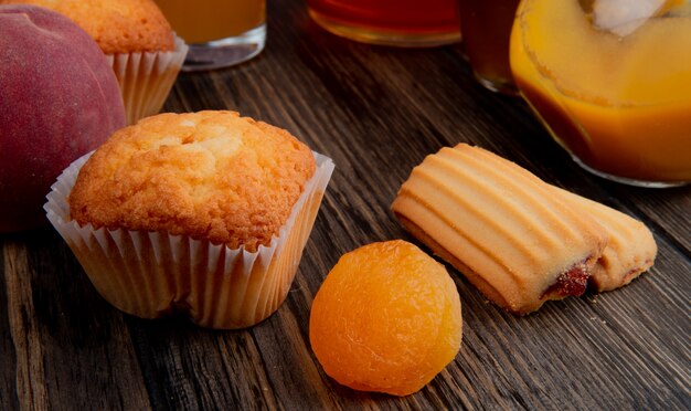 Side view of muffin with dried apricots and cookies on rustic wood