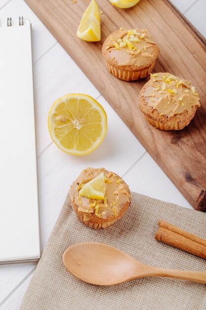 Side view muffins with half a lemon on a blackboard with a spoon and a notebook on a white surface