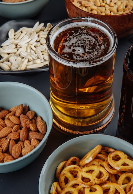 黒のスナックピーナッツヒマワリの種アーモンドとミニプレッツェルとビールのジョッキの側面図