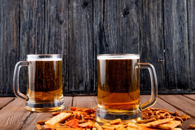 side view Mugs of beer with hard chuck chips and crackers on wooden table