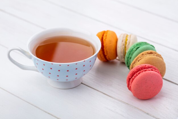 Side view of multi-colored macarons with a cup of tea on a white surface