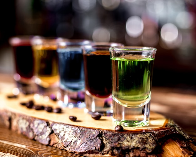 Free photo side view multi-colored shots with coffee beans on a piece of wood