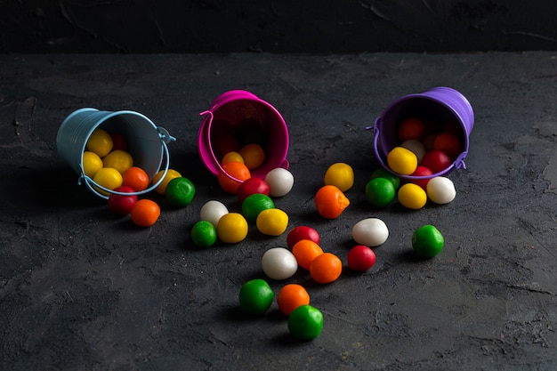 Side view of multicolor chocolate candies scattered from small buckets on black