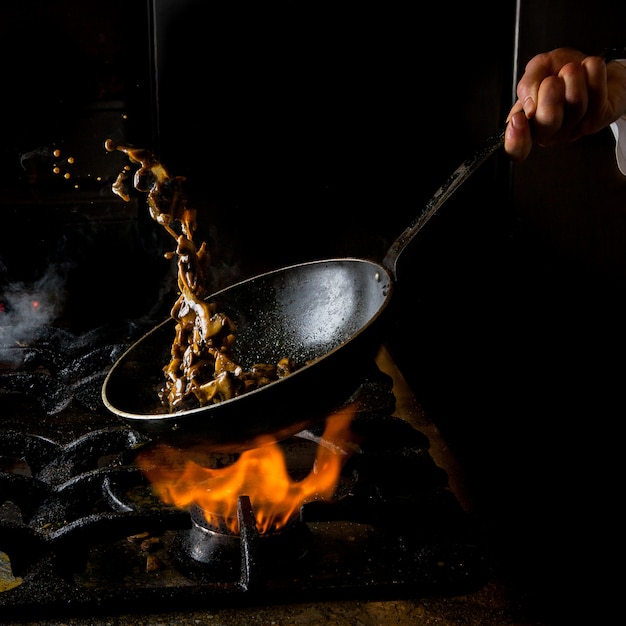 Side view mushroom frying with gas stove and fire and human hand in pan