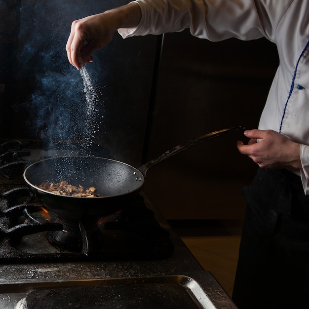 Side view mushroom frying with salt and fire and human hand in pan